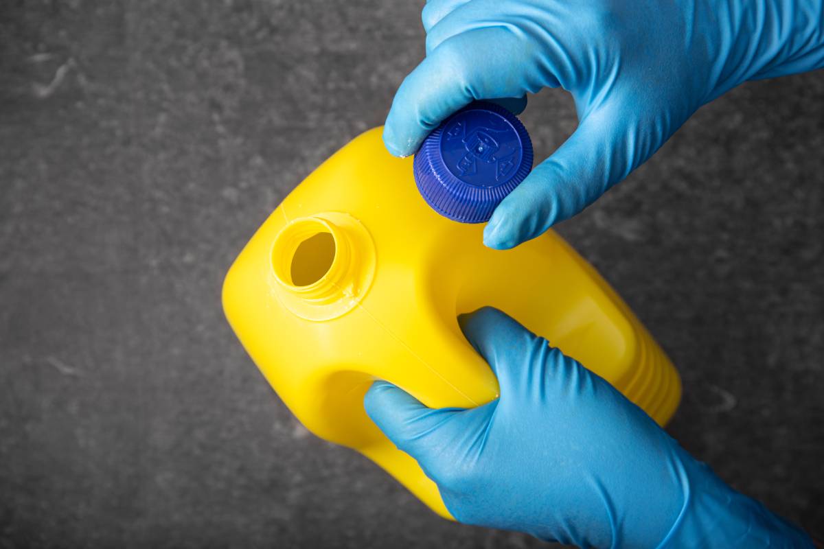 Human hand in protective glove opening a yellow bleach bottle. Disinfection concept