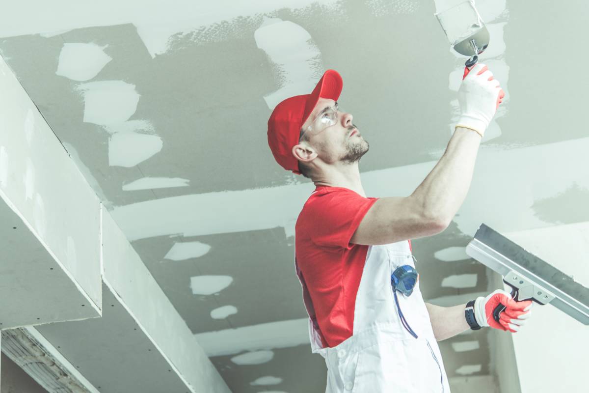 Construction and Remodeling Worker in His 30s Wearing Red Uniform Patching Drywall Ceiling Inside Remodeled Apartment.