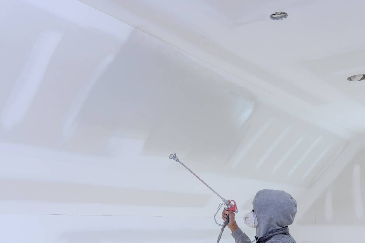 Worker uses a spray gun with a primer to paint the walls and ceilings of new home